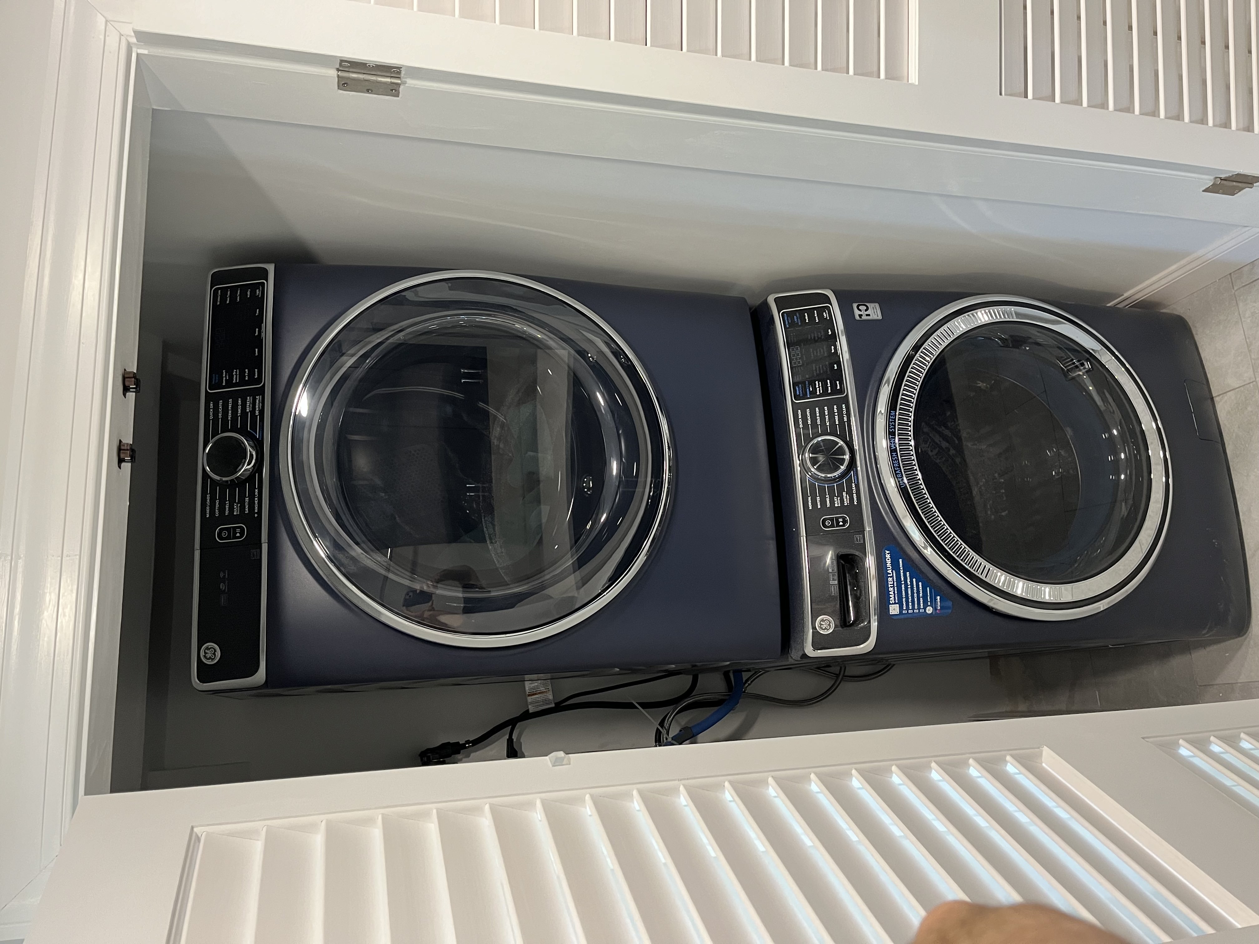 Laundry room remodel featuring a modern stacked GE washer and dryer in a built-in closet with white louvered doors and updated flooring for a clean, space-saving design.