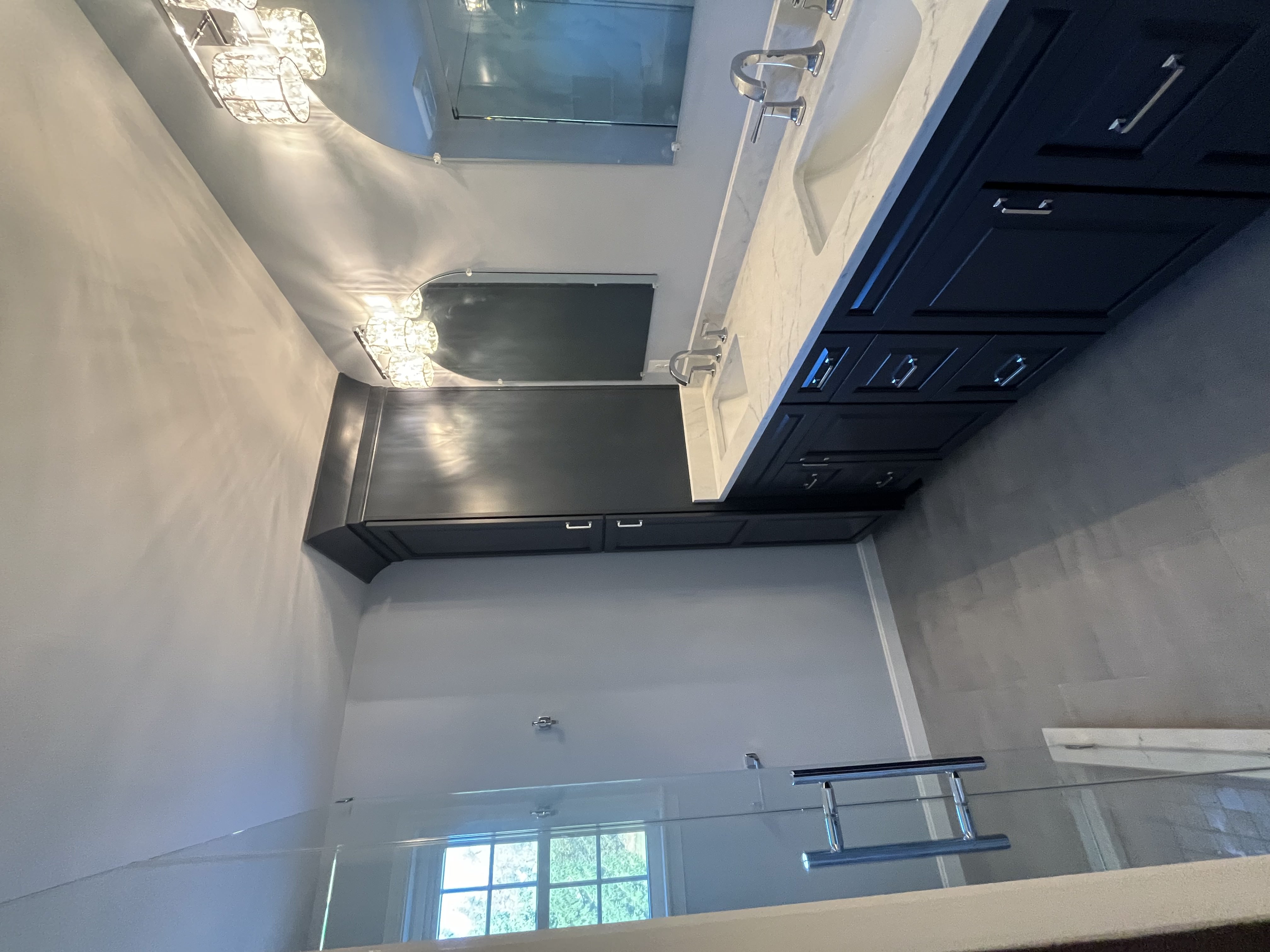 Contemporary bathroom remodel featuring a navy double vanity with marble countertop, chrome fixtures, glass shower enclosure, and modern lighting for a clean sophisticated design.