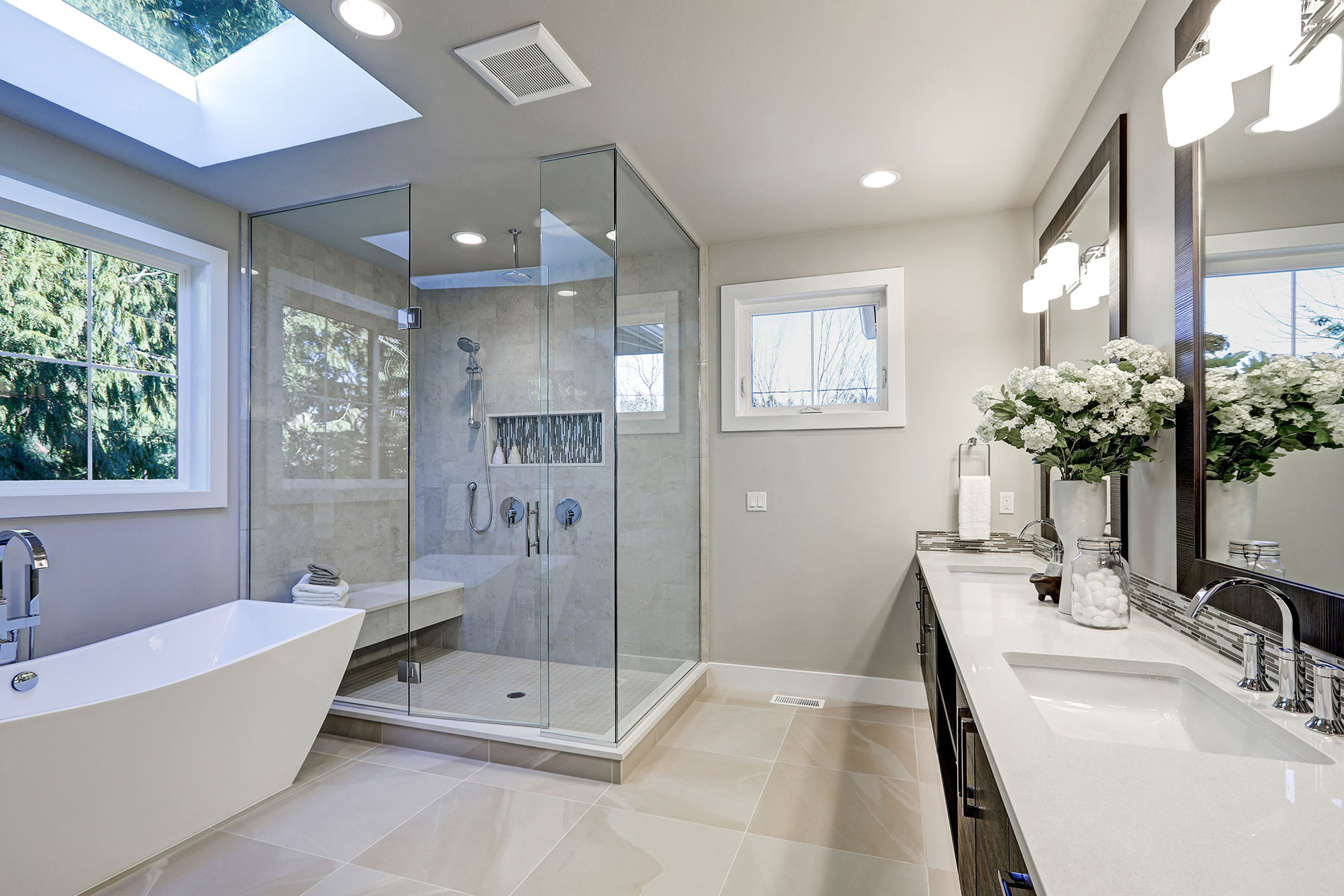 Modern luxury bathroom remodel featuring a frameless glass shower with built-in bench, freestanding soaking tub, double vanity with quartz countertops, and large windows for natural light.