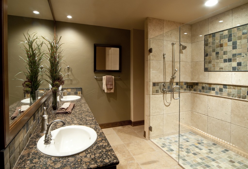 Elegant bathroom remodel featuring a glass-enclosed walk-in shower with natural stone tile and mosaic accents, granite countertop double vanity, and warm ambient lighting for a spa-like feel.