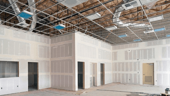 Commercial construction project showcasing interior framing, drywall installation, exposed ceiling grid, and HVAC ductwork during a building renovation phase.