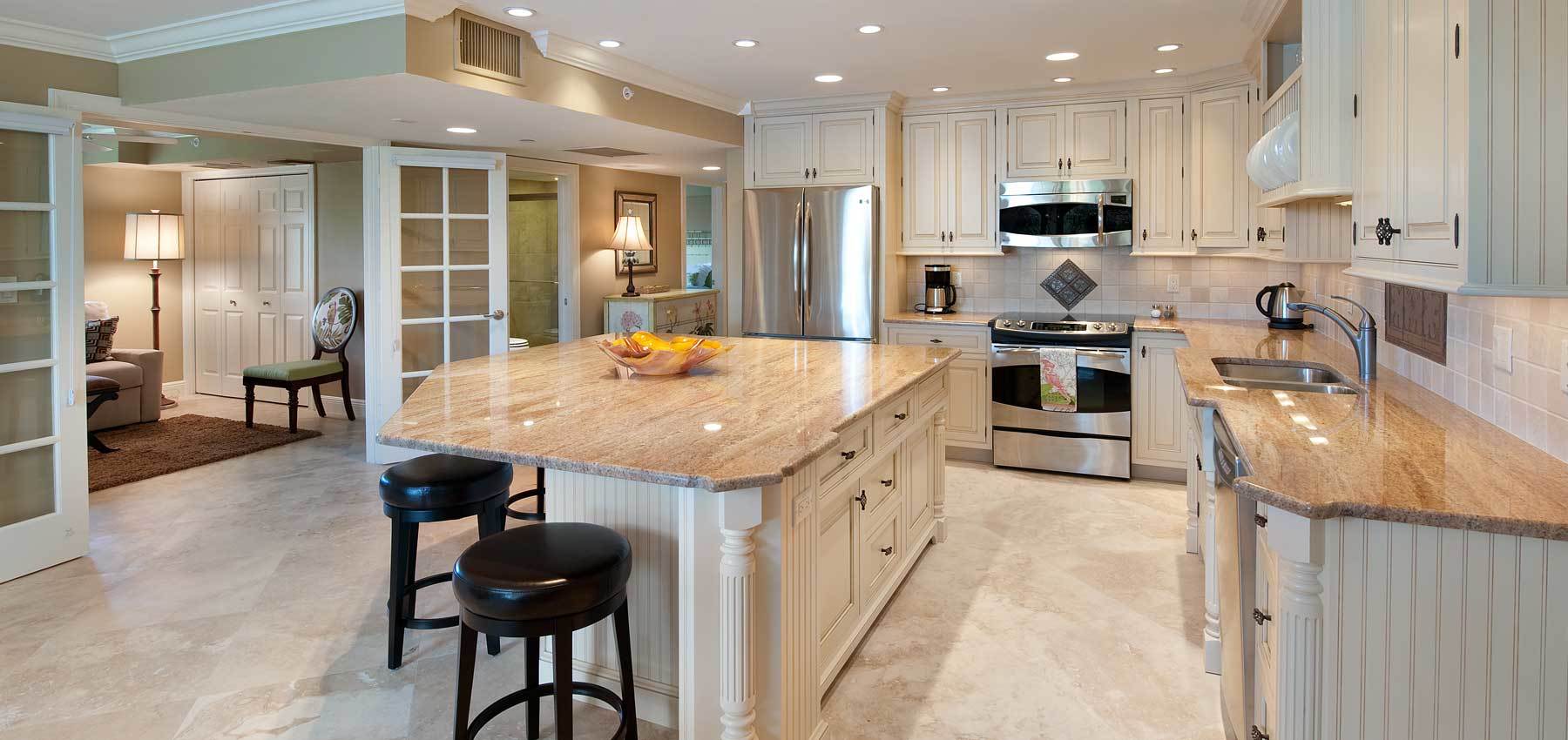 Spacious traditional kitchen remodel featuring cream cabinetry, stainless steel appliances, large granite island with seating, and open layout connecting to living area for a warm, inviting design